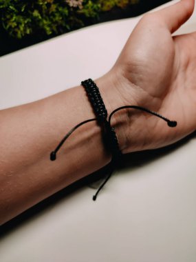 Siyah örülmüş shamballa bileziği. Kadının bileğinde sürgülü kapak var. Beyaz siyah arka plana yakın. El yapımı mücevherler, DIY fikirleri. Bohem tarzı aksesuar, tasarım 