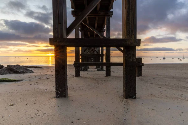 Plage des Dames, sahil iskelesinin yıpranmış ahşap destekleri arasında bir deniz gündoğumu parıldıyor, pürüzsüz kumun üzerine uzun gölgeler bırakıyor. Gemiler sakin sularda yüzerek sakin bir sahil manzarası yaratırlar..