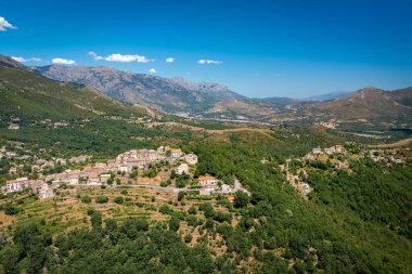 Yeşil orman ve tarlalarla çevrili, teraslı tepelerin arasına kurulmuş bir dağ köyünün yüksek manzarası.