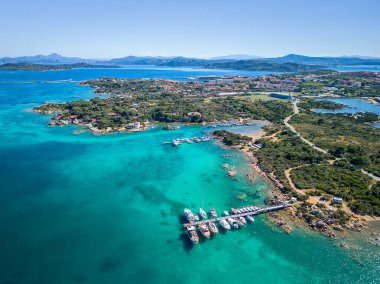 Küçük bir marina, yelkenli ve yemyeşil yeşillik içeren turkuaz bir sahil adasının havadan görünüşü. Sardunya, İtalya