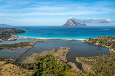 Turkuaz bir deniz, uzak volkanik ada ve doğal lagünlerden oluşan nefes kesici bir kıyı manzarası, Sardunya, İtalya