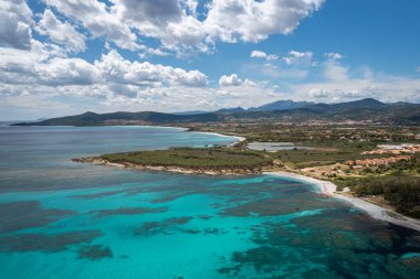 İnsansız hava aracı turkuaz deniz, beyaz kumlu plajlar, yemyeşil bitki örtüsü ve uzak dağlar, Sardunya, İtalya ile canlı bir kıyı manzarası yakalar.