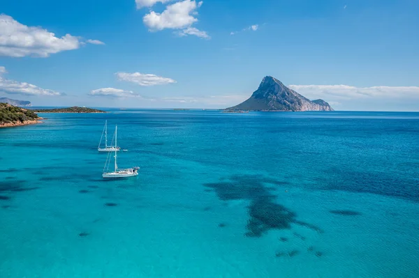 Sakin bir sahil sahnesi, İtalya 'nın uzak bir adası olan Sardunya' da berrak turkuaz sulara demir atmış beyaz bir yelkenliyi gösteriyor.