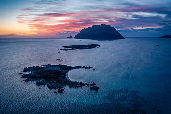 Alacakaranlıkta sakin bir sahil sahnesinde uzak bir ada, mavi deniz ve pastel gökyüzü, Sardunya, İtalya
