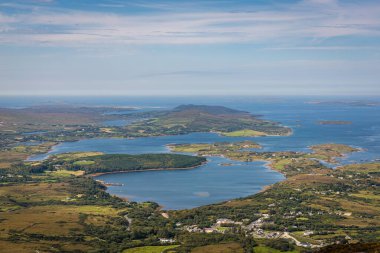 Adaların, körfezlerin ve yemyeşil tepelerin bulunduğu geniş bir kıyı bölgesi manzarası. Sakin mavi sular, küçük köyler, Connemara, İrlanda
