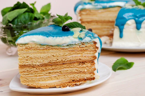 Piece of cake decorated with blue cream, mint and blueberries on