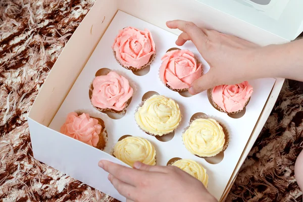 Cupcakes con crema rosa y amarilla en caja de papel sobre fondo marrón — Foto de Stock