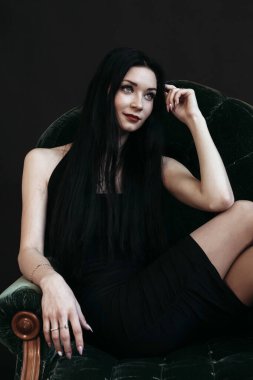 İnce esmer kadın kanepede oturuyor. Yeni yıl arifesi, karanlık arka plan..