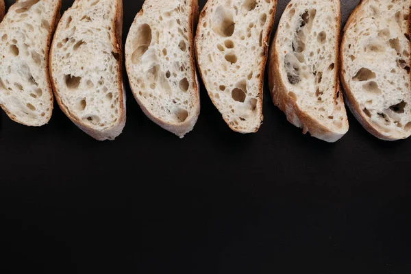 Sliced ciabatta bread on black background. Italian white bread. Top view with copy space.