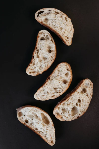 Sliced ciabatta bread on black background. Italian white bread. Top view.