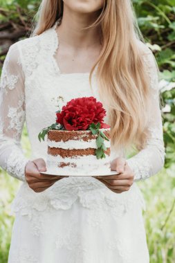 Bride in wedding dress holding beautiful delicious wedding cake. Vanilla cake with floral decoration.