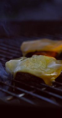 Izgara biftekli erimiş peynirin yakın çekimi. Duman ve ısı yükseliyor. Lezzetli bir barbekü anı..