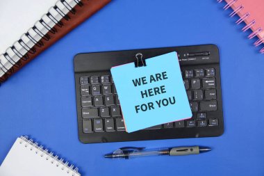 Koyu mavi yüzey üzerindeki bir klavyeye bağlanıp destek, müşteri hizmetleri, uzaktan yardım, ofis iletişimi ve teşvikle ilgili mavi yapışkan not..