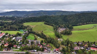 Etkileyici bir hava manzarası sergileniyor yemyeşil tepeler ve bulutlu gökyüzünün altında yuva yapmış büyüleyici evler.