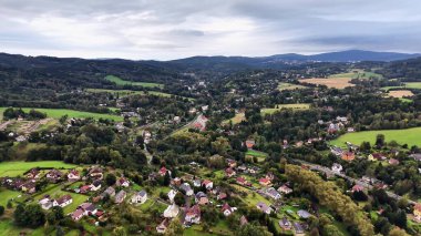 Bu hava manzarası, büyüleyici evleri ve yuvarlanan tepeleri olan canlı bir kırsal bölgeyi gösteriyor. Resmedilmeye değer bir manzara oluşturuyor.