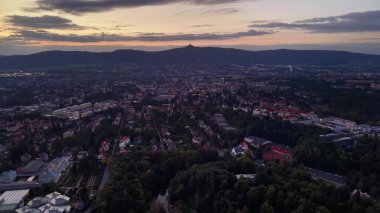 Resimli bir günbatımının çarpıcı hava manzarası, canlı bir şehir manzarasını sergiliyor, arka planda verimli tepeler var.