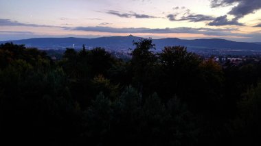 Güzel bir günbatımı canlı bir şehrin üzerine sıcak bir ışık saçar, yemyeşil ağaçlar ve şehir yaşamını uyum içinde harmanlar.