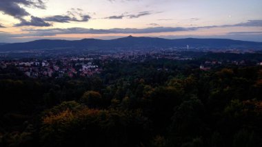 Büyüleyici bir şehir manzarası güzel bir şekilde sergileniyor yemyeşil bir vadi ve şehrin ufuk çizgisi muhteşem bir günbatımında
