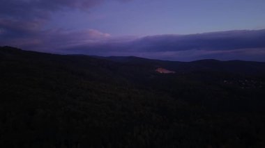 Nefes kesici ve büyüleyici alacakaranlık manzarası sakin bir orman zeminiyle süslenmiş yuvarlanan tepeleri gösteriyor.