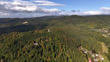 Göz kamaştırıcı hava manzarası, berrak mavi gökyüzünün altında yemyeşil ormanlar ve görkemli tepeler sergiliyor.