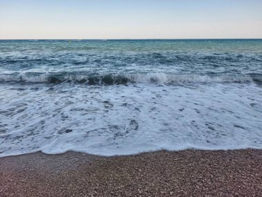 Gentle waves are lapping softly at the shore, creating a serene and tranquil seaside atmosphere that enchants