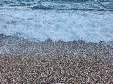 Gentle waves continuously lap at a pebbled shore, creating a beautifully serene coastal atmosphere all around