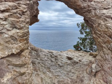 A breathtakingly picturesque view of the vast ocean framed beautifully by a natural rocky arch and a cloudy sky