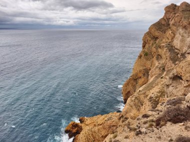 Kayalık kayalıkların nefes kesici ve çarpıcı manzarası bulutlu bir gökyüzünün altında sakin okyanusla çarpışıyor.