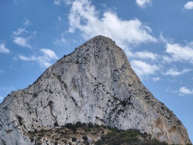 Tüylü bulutların güzel zeminine karşı yükselen, nefes kesici bir dağ zirvesi manzarası.