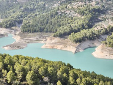 A stunning and picturesque view of a beautiful turquoise reservoir surrounded by lush, vibrant green trees