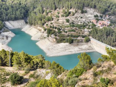 A breathtaking and stunning view of a tranquil reservoir beautifully nestled among lush, verdant hills and tall trees