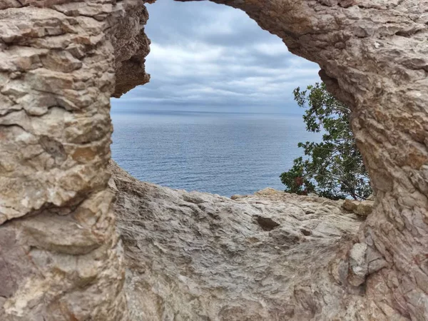 A breathtakingly picturesque view of the vast ocean framed beautifully by a natural rocky arch and a cloudy sky