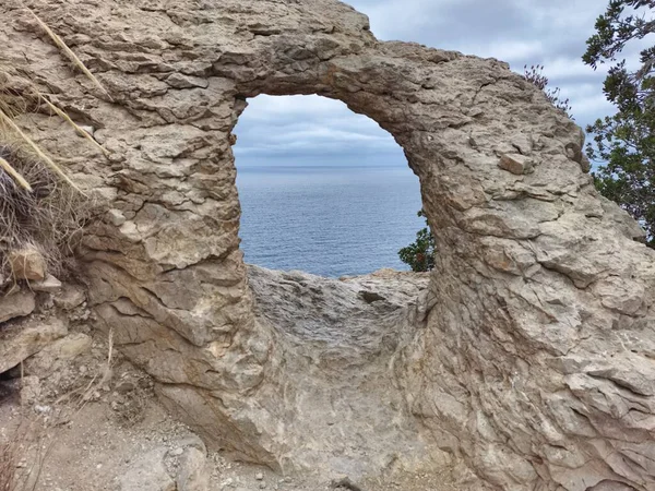 A natural rock arch frames a breathtaking view of the ocean horizon, showcasing stunning geological beauty