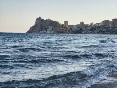 A serene view of majestic waves and a coastal city against a rocky backdrop at dusk, creating tranquility