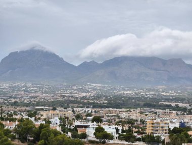 A scenic view of majestic mountains shrouded in soft clouds, overlooking a peaceful town nestled below