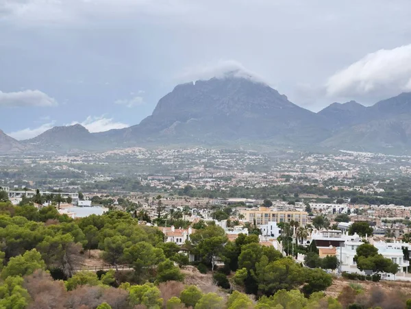 A breathtaking view features a stunning mountain surrounded by vibrant urban areas and lush greenery under cloudy skies