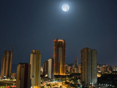 Dolunay tarafından aydınlatılmış büyüleyici bir ufuk çizgisi, gece gökyüzünde çarpıcı modern mimari sergileniyor.