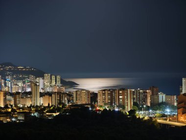 Şehir ışıkları ve okyanus yansımalarıyla parıldayan kıyı şehrinin çarpıcı gece manzarasına tanık olun.