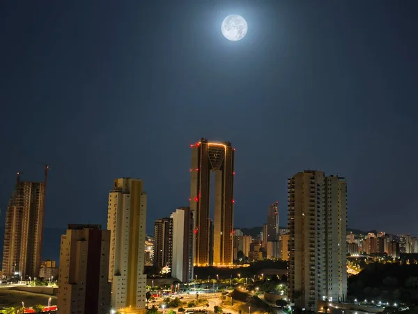 Dolunay tarafından aydınlatılmış büyüleyici bir ufuk çizgisi, gece gökyüzünde çarpıcı modern mimari sergileniyor.