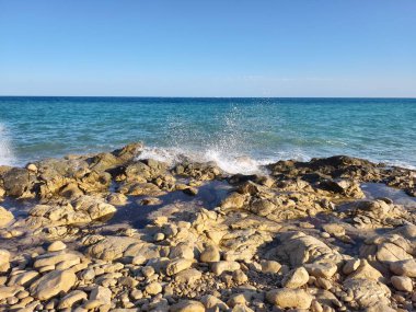 A breathtakingly serene view of the vast ocean gracefully meeting rocky shores beneath a clear blue sky
