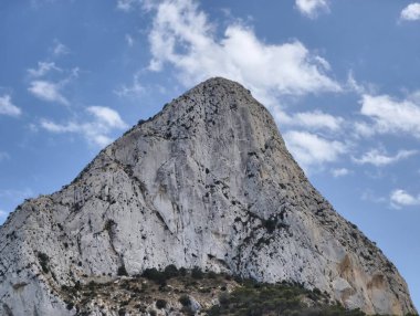 Tüylü bulutların güzel zeminine karşı yükselen, nefes kesici bir dağ zirvesi manzarası.