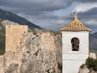 Dramatik dağ manzaraları karşısında eski bir şatonun ve büyüleyici çan kulesinin çarpıcı manzarası.