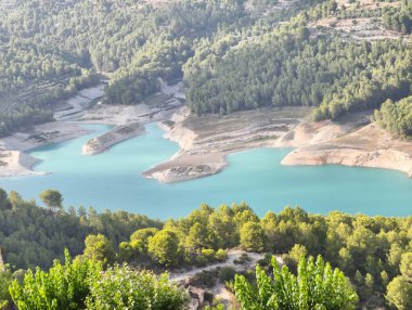 Hava manzarası, yemyeşil tepelerle çevrili çarpıcı bir turkuaz göl gösteriyor.