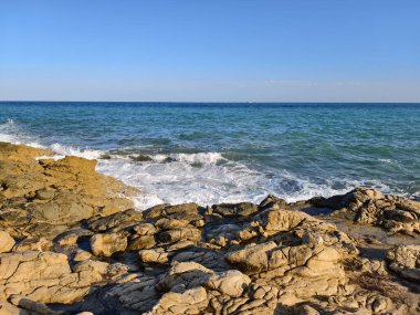 Yoğun bir okyanus görüntüsü güçlü dalgaların dinamik bir şekilde kayalık kıyılara çarptığını gösteriyor.
