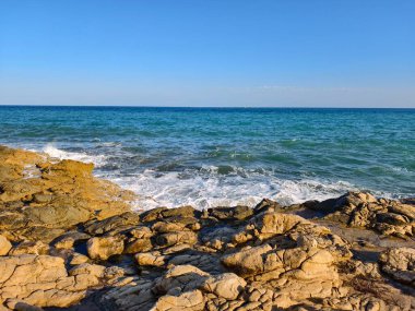 Kayaların ve dalgaların ötesindeki engin açık deniz ufku özgürlük ve sükuneti çağrıştırıyor.