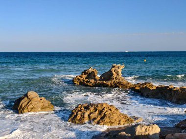 Yıpranmış kayaları vurgulayan güzel bir akşam ışığı ve manzaralı seyahat görüntüleri için sakin dalgalar.