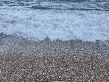 Köpük ve taşlarla sörfe yakın çekim, köpük çizgileri ve yumuşak dalgalarla sakin sahil manzarası