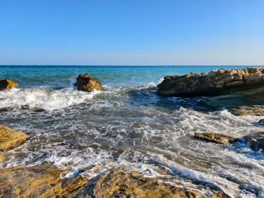 Parlak turkuaz sular ve uzak ufuk, turkuaz deniz kayalıkların üzerinde güneş ışığı dokularıyla çağlıyor.