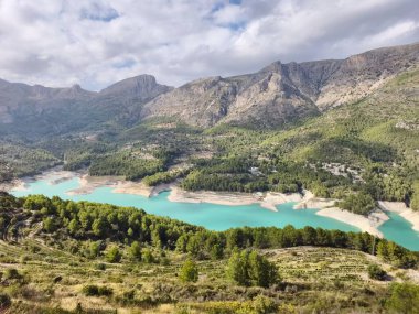 Sarmal turkuaz rezervuar sürüklenen bulutların altındaki yemyeşil vadide yol alır.