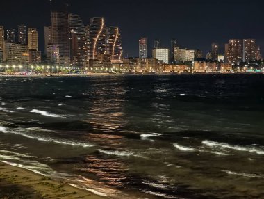 Dalgalar ve uzak ışıklarla sakin deniz manzarası, dalgalı dalgaların olduğu gece okyanus manzarası